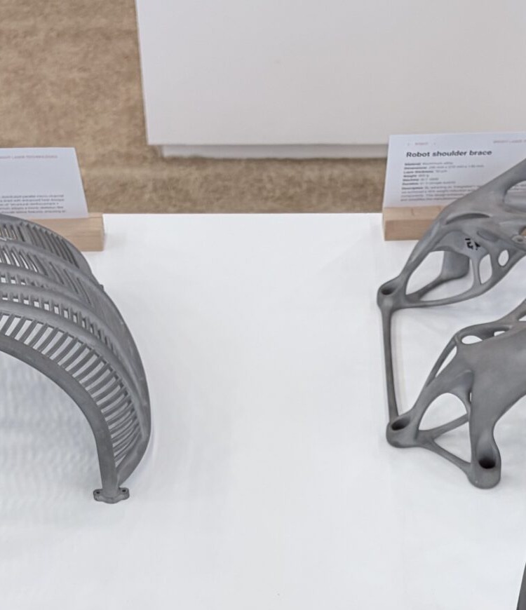Metal additive robot shoulder brace displayed beside a slotted arched fin coupon