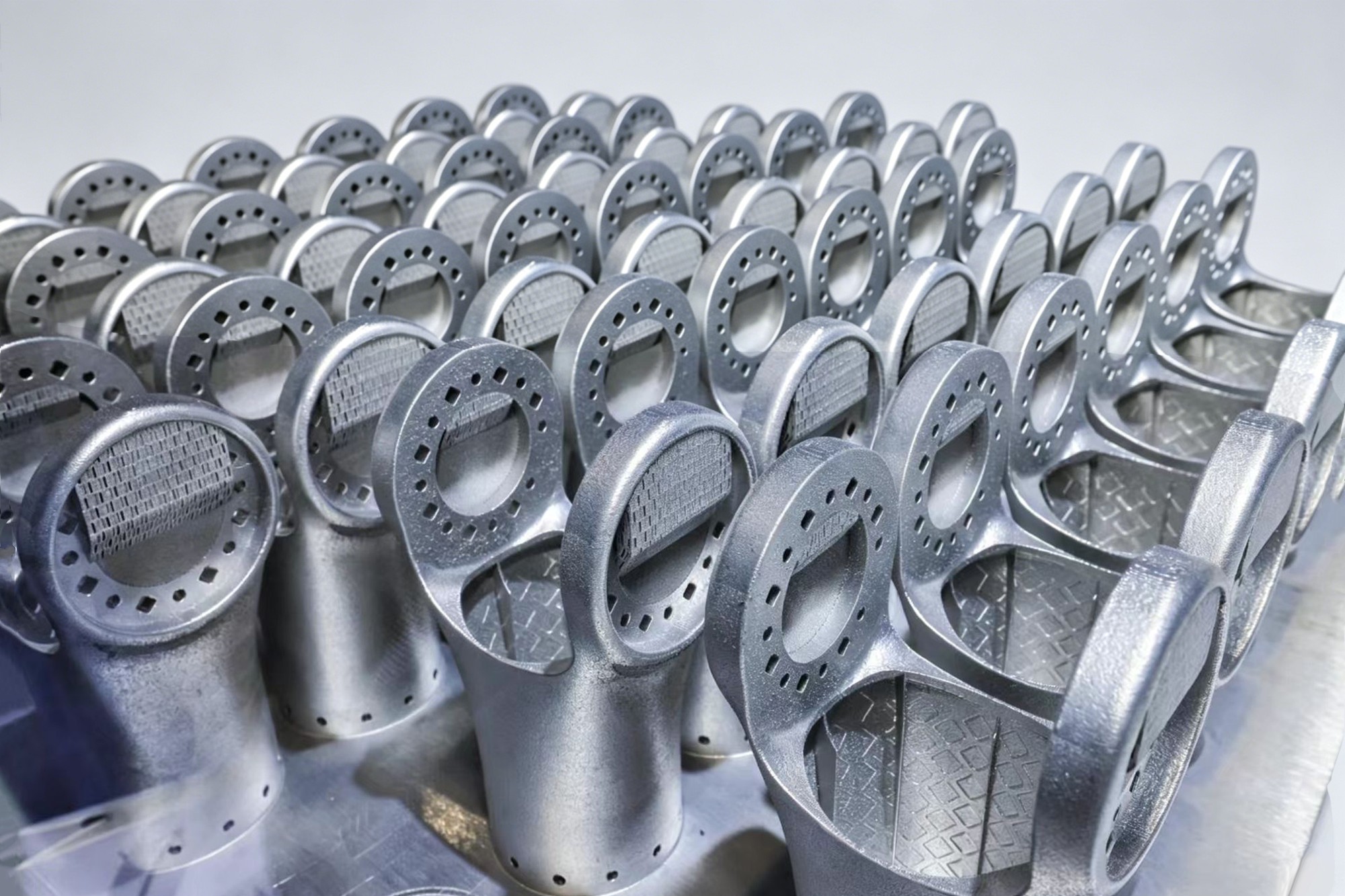 Rows of metal AM robot arm shells nested on a powder-bed build plate
